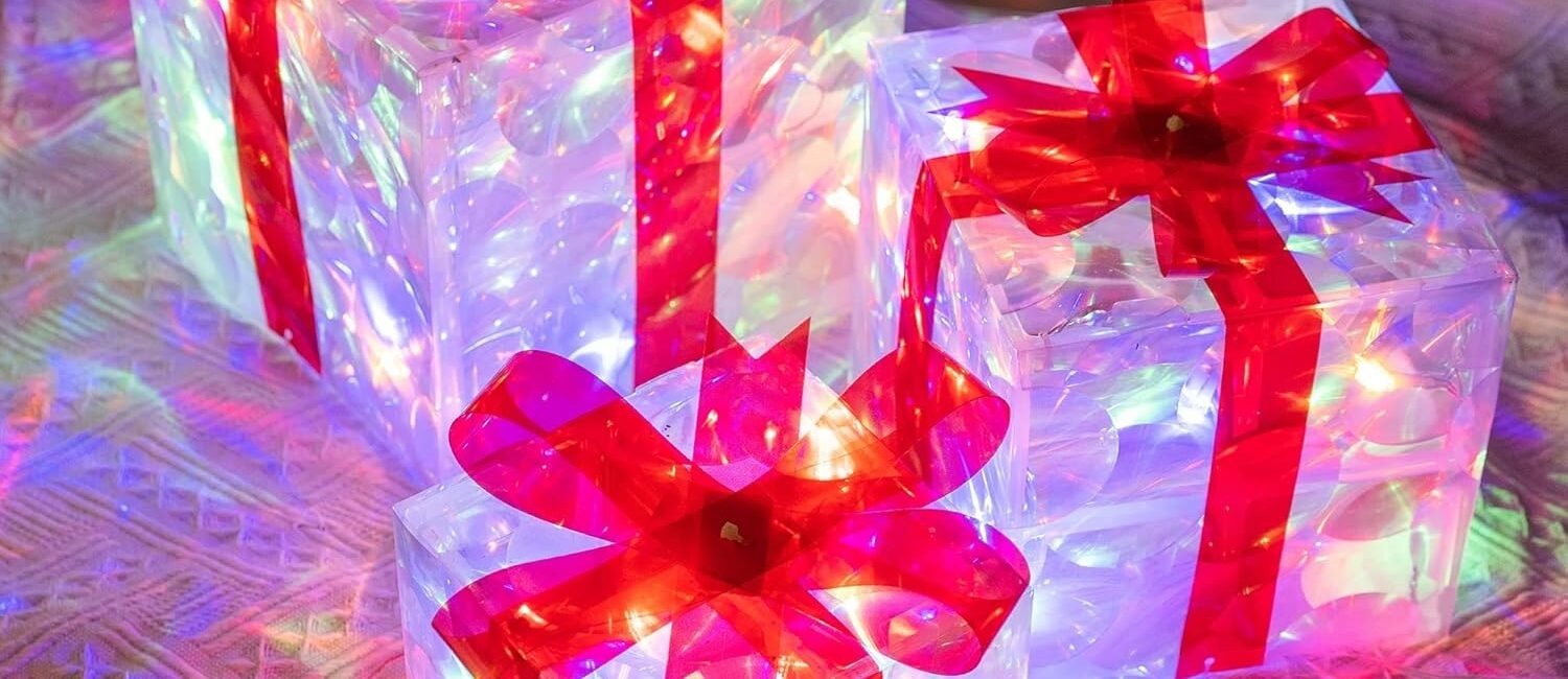 Multicolor lighted Christmas gift boxes with red bows and LED lights glowing indoors on a festive background.