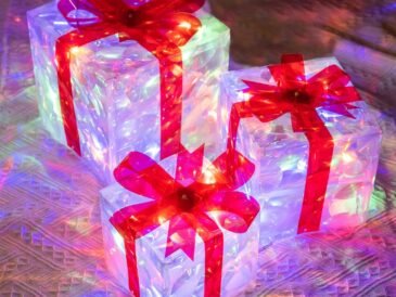 Multicolor lighted Christmas gift boxes with red bows and LED lights glowing indoors on a festive background.