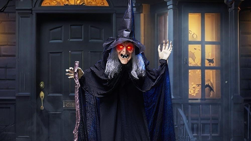 Life-size Halloween witch prop with glowing eyes and cane for outdoor yard decoration.