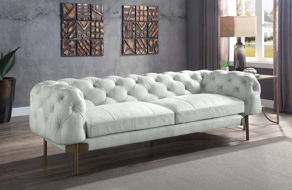 Vintage white Chesterfield sofa with tufted leather and metal legs.