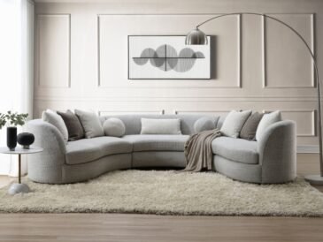 Curved gray boucle sectional sofa with feather-filled pillows in a modern neutral living room setting.