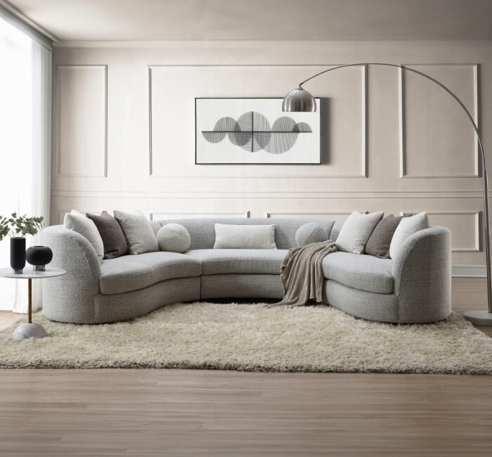 Curved gray boucle sectional sofa with feather-filled pillows in a modern neutral living room setting.