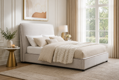 Pacifico upholstered bed with light neutral fabric, curved headboard, warm brown trim, cream bedding, and a textured rug in a bright modern bedroom.